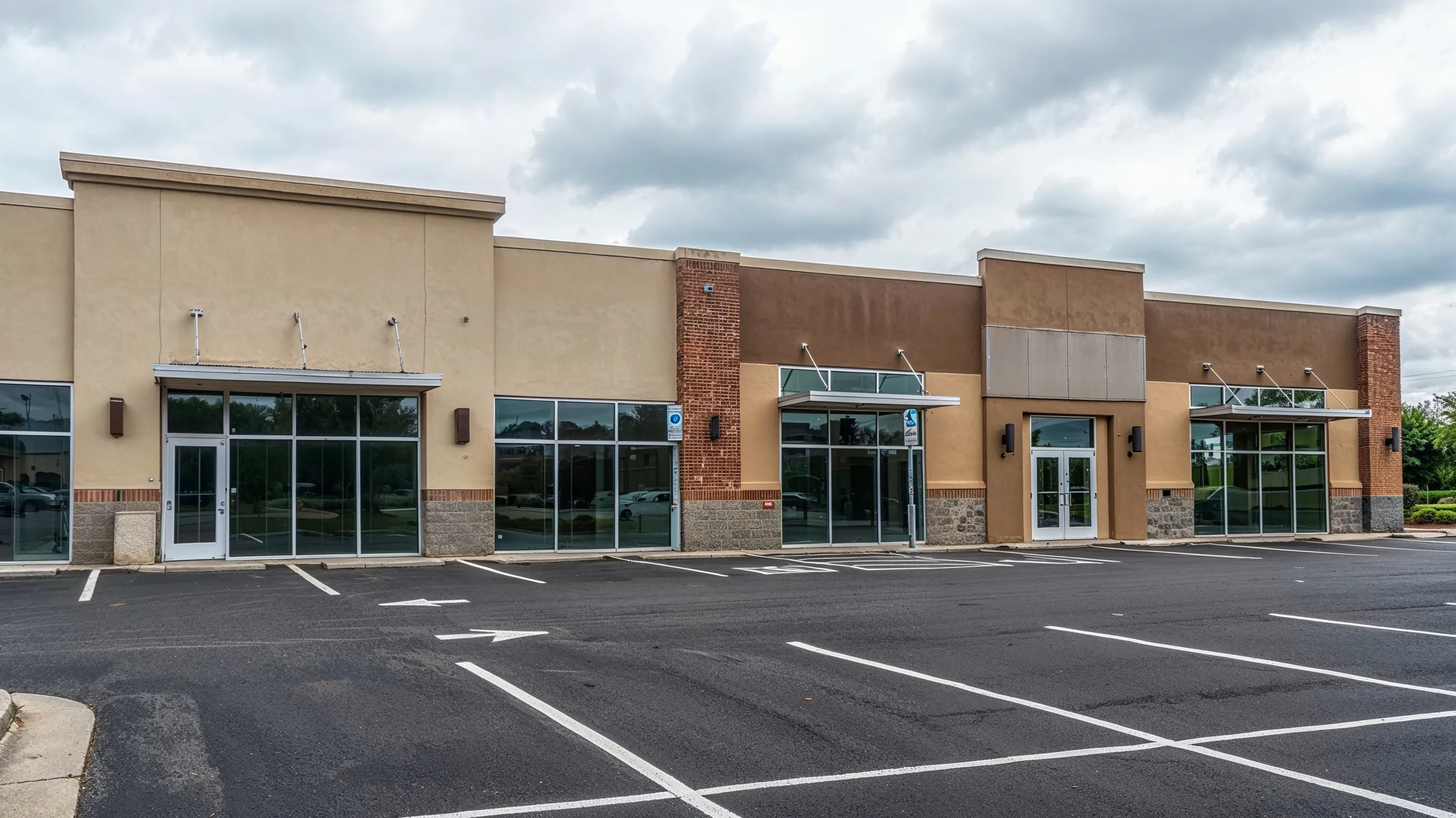 Before photo of commercial remodeling project in Los Angeles with older retail building exterior, beige storefront facade, glass entrances, parking lot, and business property before renovation